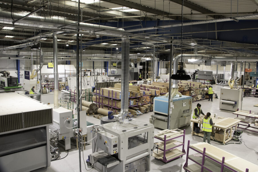 Interior view of a manufacturing facility with various woodworking machinery and stacks of wooden materials.